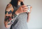 femme au bras tatoué buvant un café