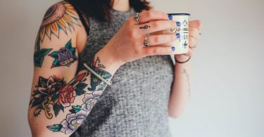 femme au bras tatoué buvant un café