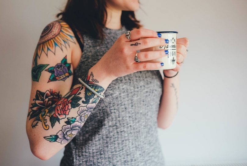 femme au bras tatoué buvant un café