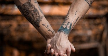 Deux personnes se tenant la main, et ayant les bras tatoués.