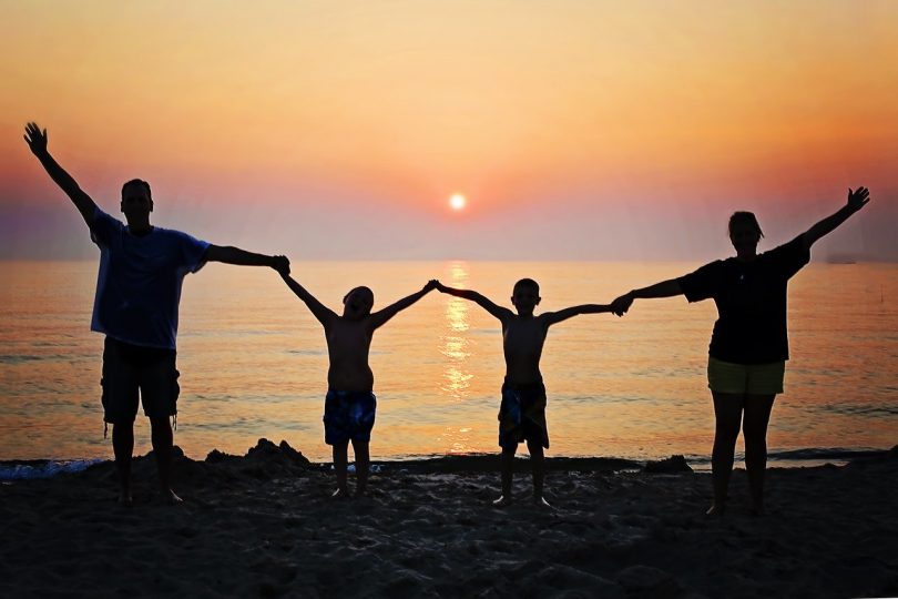 famille les bras levés devant la mer au coucher du soleil